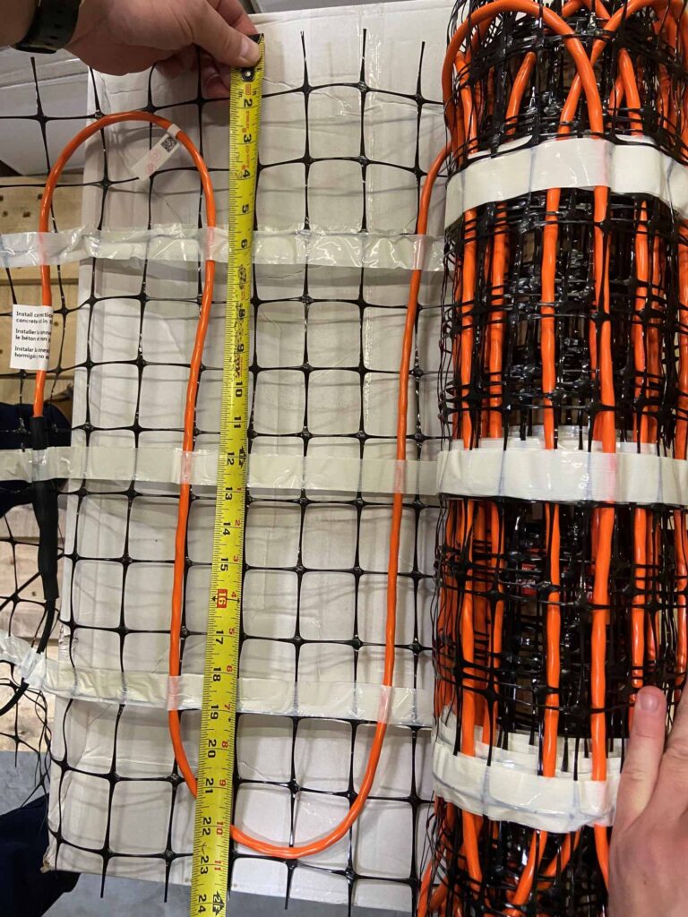 Hands measuring spacing on in-slab radiant heat cables embedded in mat