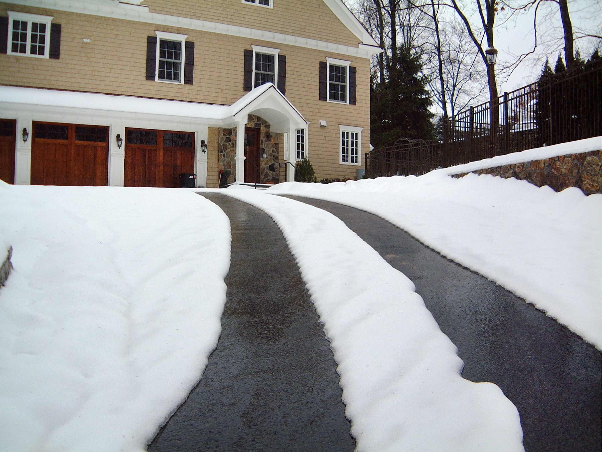 Tan two-story house. A snow-covered driveway with melted tire tracks leads up to the front of the house.