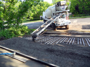 Asphalt being poured from truck over a driveway laid with radiant heating cables.