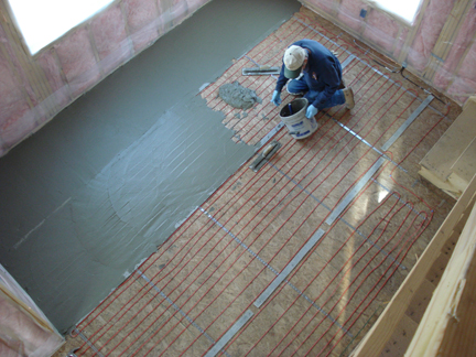Man pouring Thinset over heat cable laid out over wood subfloor