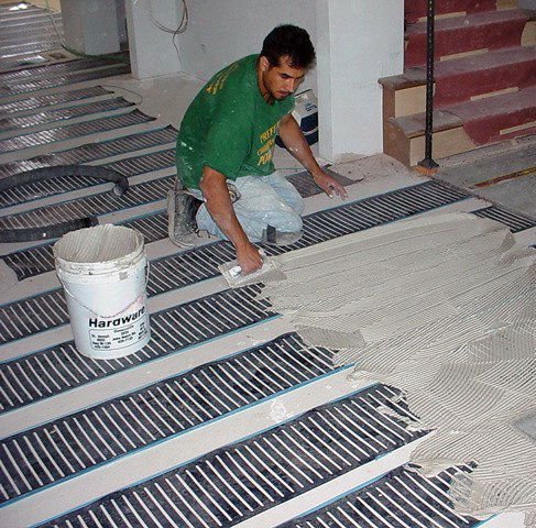 man pouring thinset over floorheat step