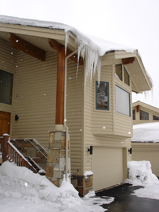 Home with dangerous icicles and roof ice over sidewalk, in need of a roof de-icing system