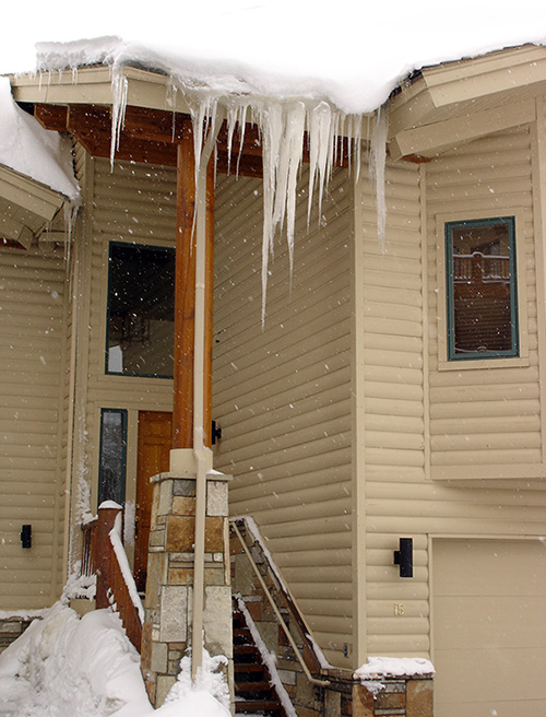 Heavy roof snow and ice hanging over steps and sidewalk